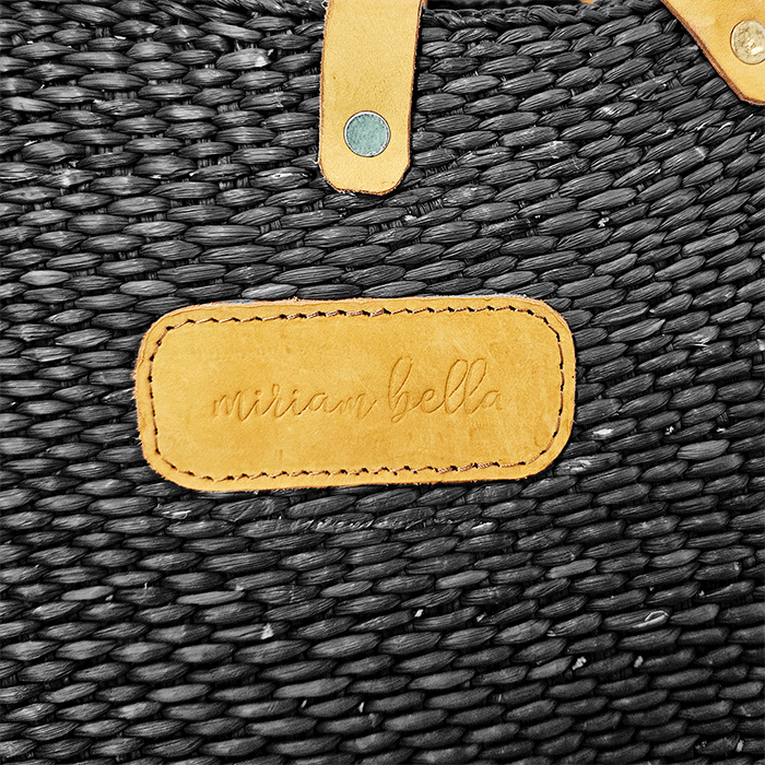 Close-up of a textured black bag with a tan leather patch displaying 'miriam bella'.