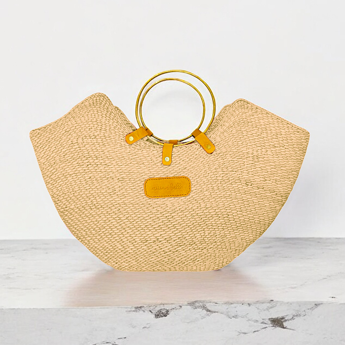A handwoven natural seagrass tote bag with brass handles, displayed on a marble surface.