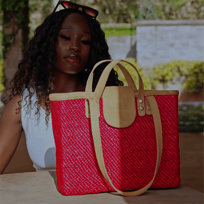Woman holding a red woven handbag with beige accents outdoors