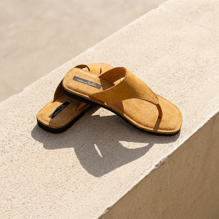 A pair of women's leather slides with wedge heel, produced by Australian brand Miriam Bella on a light surface with water in the background
