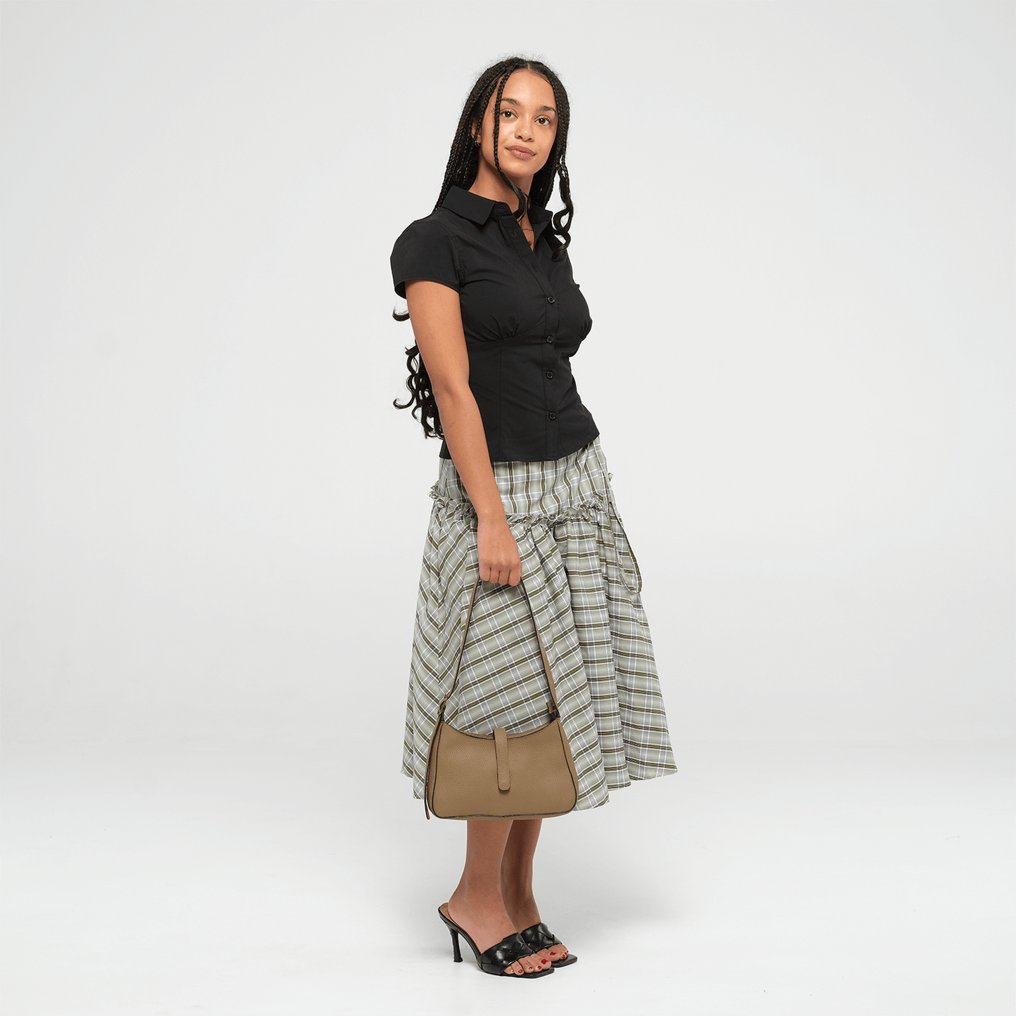 Woman wearing a black top and plaid skirt with an oIive leather mini shoulder bag on a white background