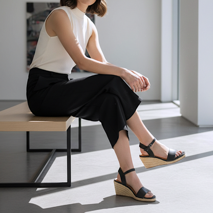 Woman sitting on a bench wearing black sandals with a white top and black pants.