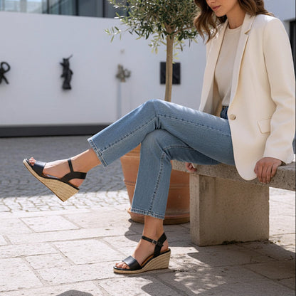 Woman sitting on a bench wearing black sandals, light blue jeans, and a cream blazer.