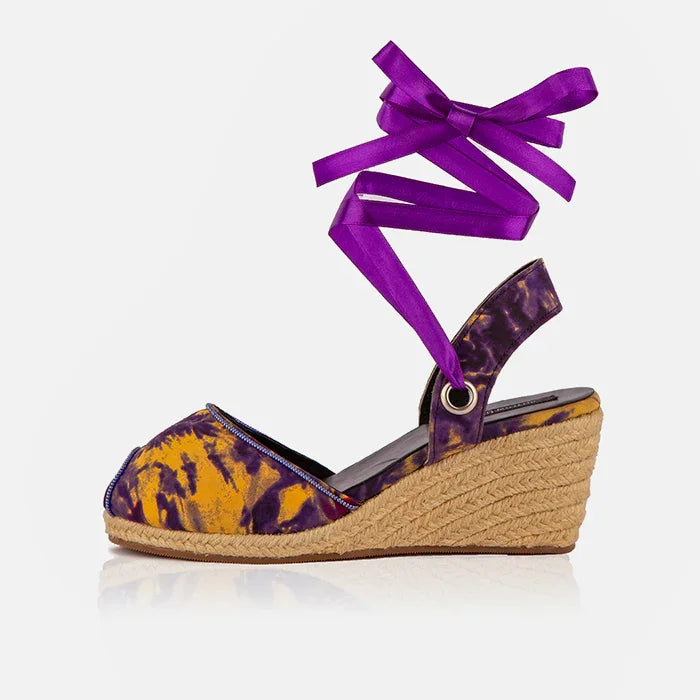 Wedge sandal with purple and yellow tie-dye pattern and a purple ribbon on a white background
