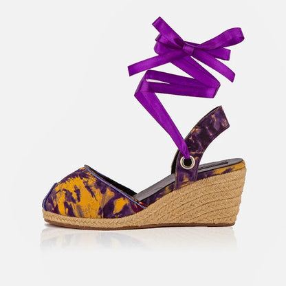 Wedge sandal with purple and yellow tie-dye pattern and a purple ribbon on a white background
