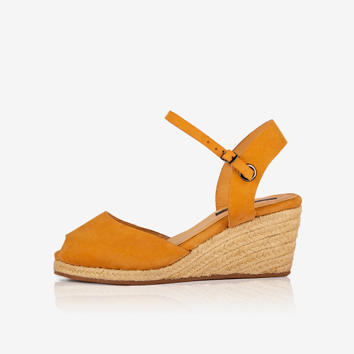 A ochre colored leather closed toe espadrille produced by australian brand Miriam Bella, with a jute-wrapped wedge heel and an adjustable ankle strap featuring a buckle.