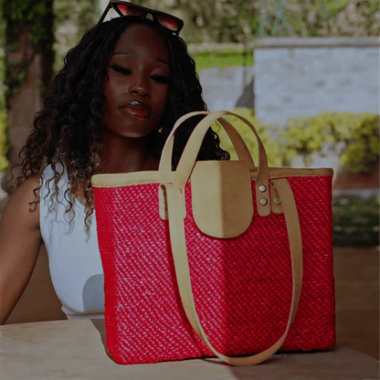 Woman holding a red woven handbag with beige accents outdoors