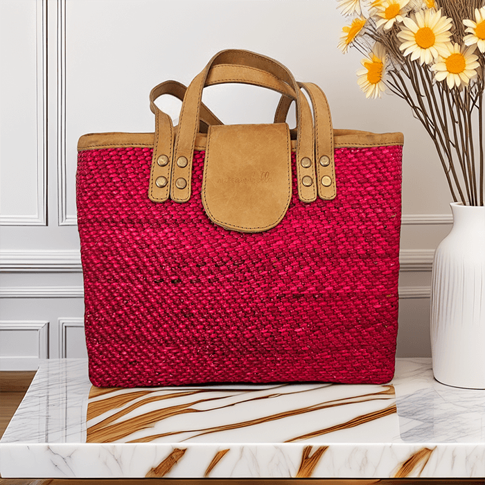 Red woven handbag with brown handles and flap on a marble surface.