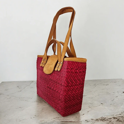 Red woven handbag with brown leather handles on a light wooden surface.