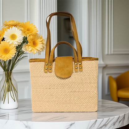 Beige woven tote bag with brown leather accents on a marble surface with yellow flowers.