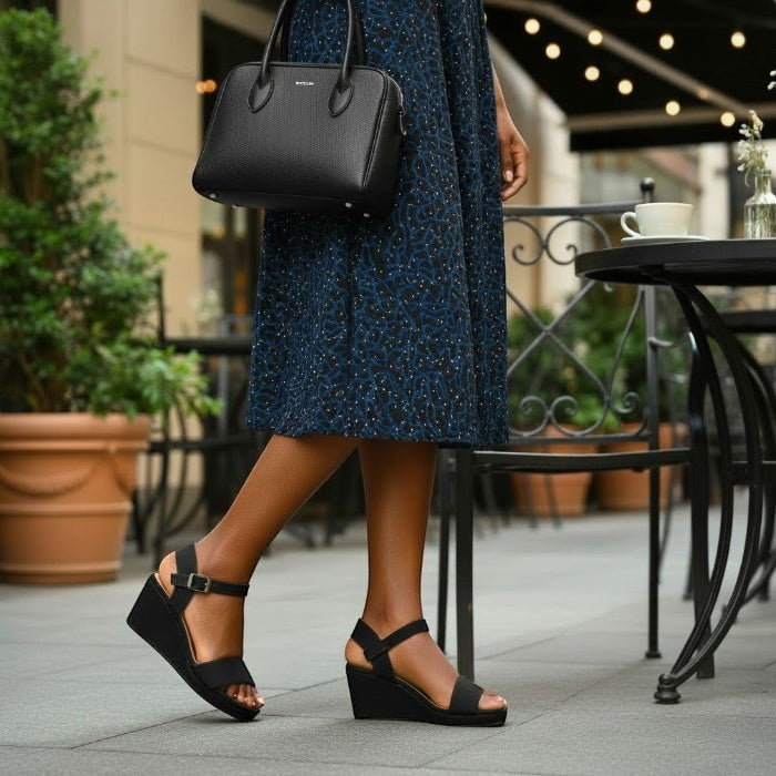 Person wearing a blue dress and black espadrille wedge sandals with a black handbag in an outdoor setting.