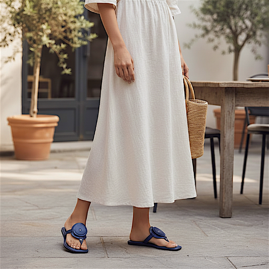 Person wearing a white dress and blue flat leather sandals standing outdoors near a wooden table.