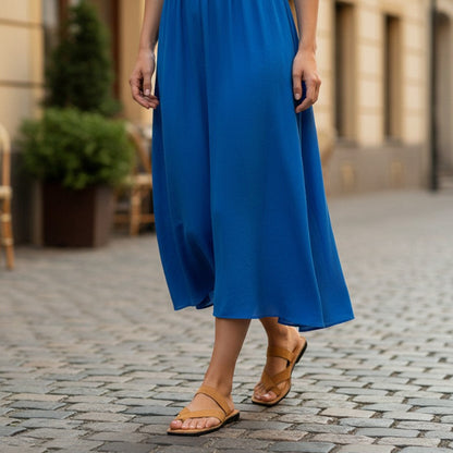 Person wearing a blue dress and tan leather sandals on a cobblestone street.