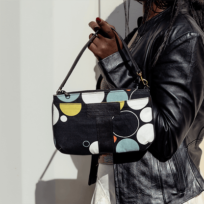 Person holding a black handbag with colorful geometric patterns against a light background