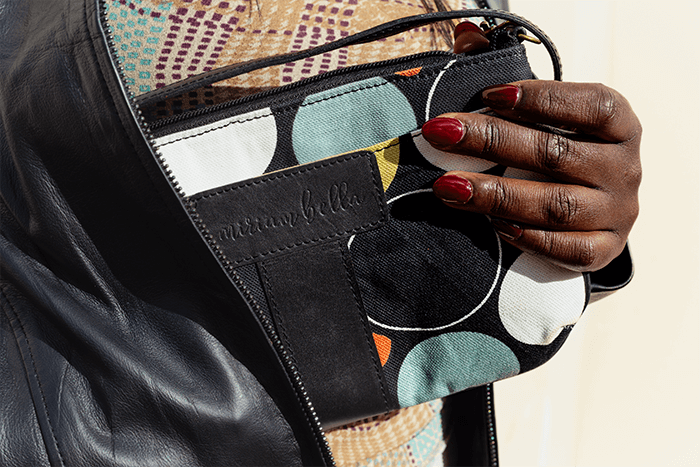 Hand holding a patterned handbag with 'Bella' branding.