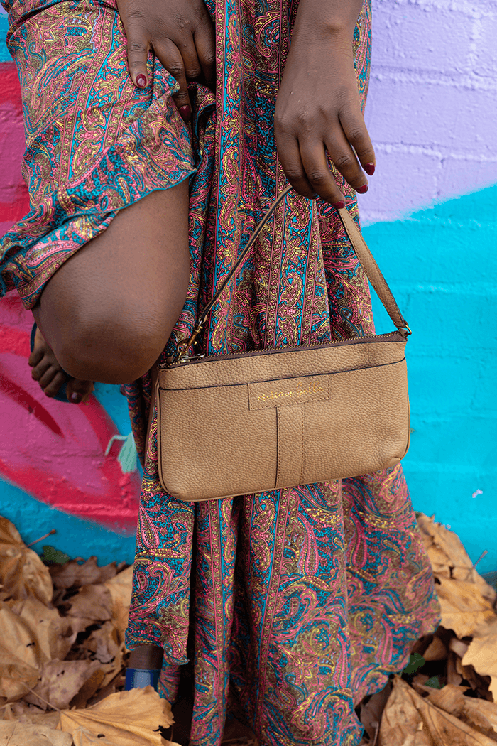 Person wearing a patterned outfit with a beige handbag against a colorful background