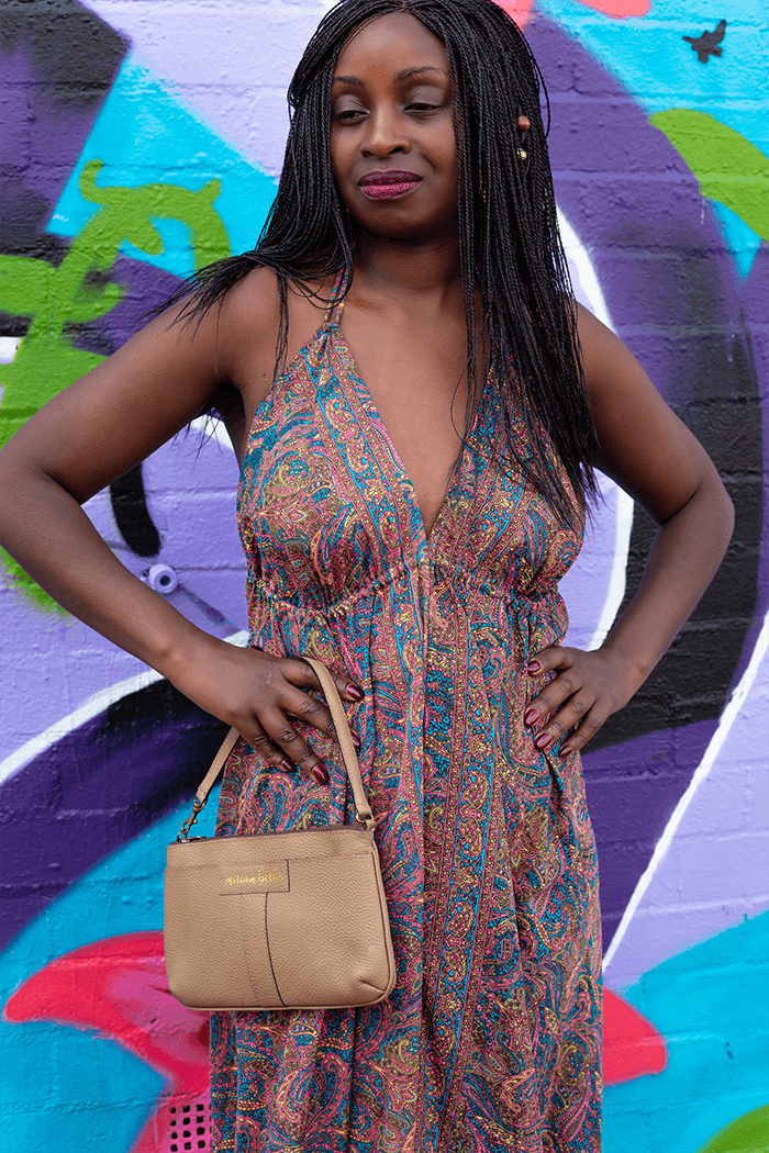 Woman in a patterned dress holding a beige handbag against a colorful graffiti wall.