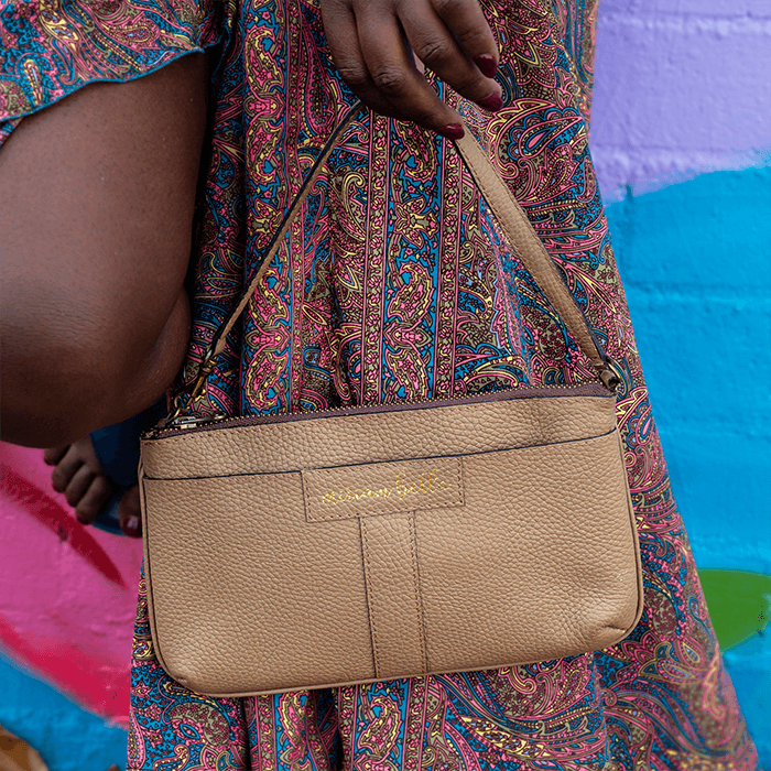 Beige handbag held by a person wearing a colorful patterned dress against a multicolored background.