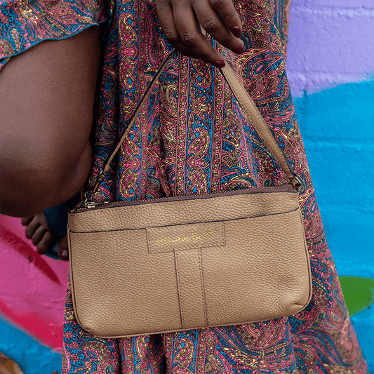 Beige handbag held by a person wearing a colorful patterned dress against a multicolored background.