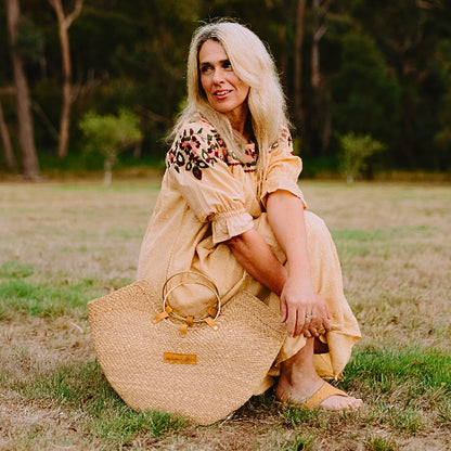 Woman in a yellow dress sitting on grass with a straw bag