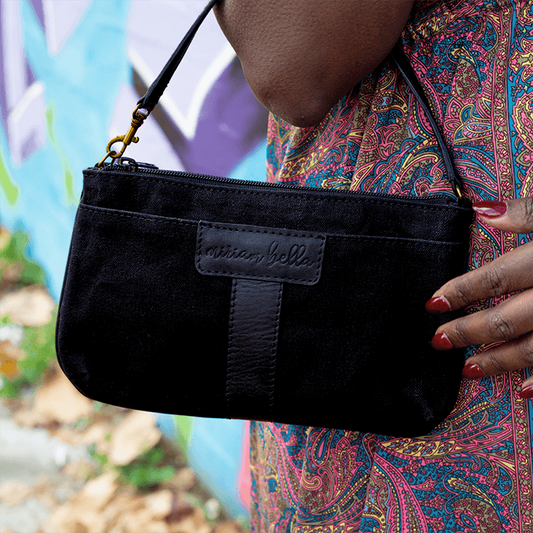 Black clutch bag held by a person with a colorful patterned garment, blurred natural background