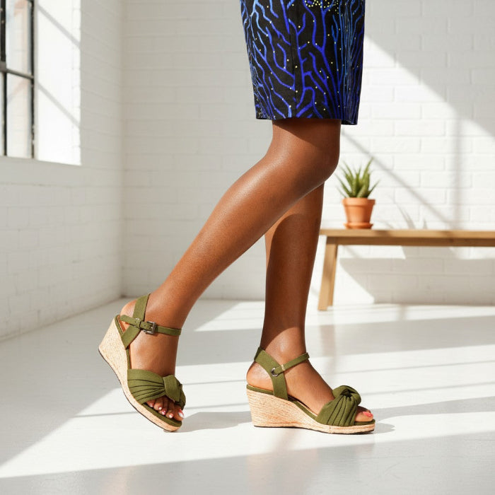 Person wearing green espadrille wedge sandals with a patterned skirt in a bright room.