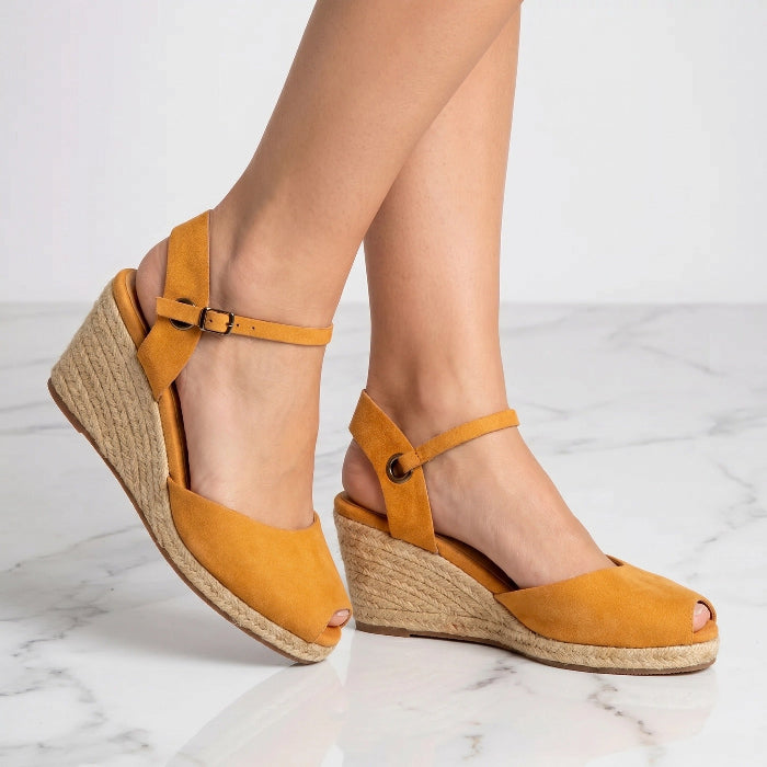 A pair of handcrafted leather ochre wedge espadrille sandals with jute sole by Miriam Bella sandals on a white marble floor