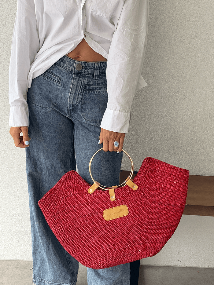 Person holding a red woven handbag with wooden handle against a neutral background