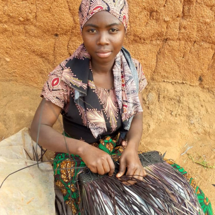 A woman wearing a patterned headwrap and matching printed waving on of woven tote bags from the Miriam Bella collection.