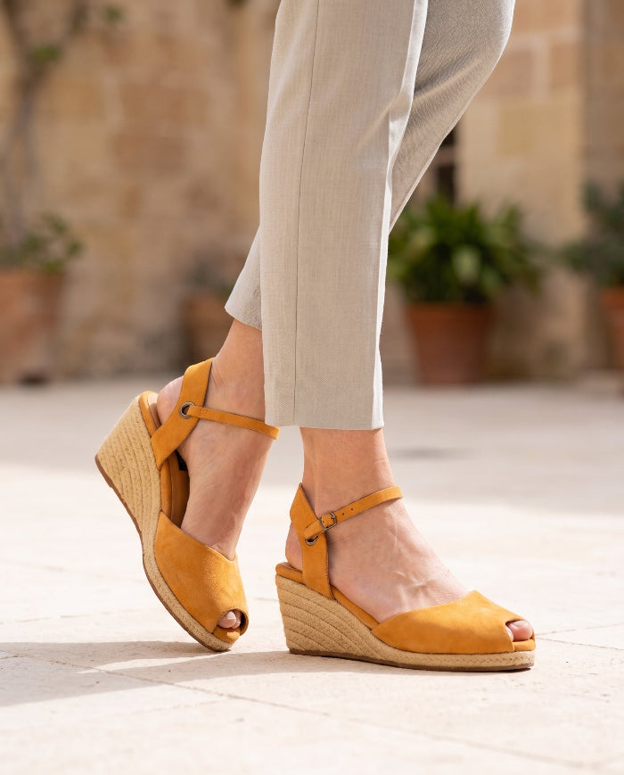 A pair of handcrafted leather ochre wedge espadrille sandals with jute sole by Miriam Bella sandals in a courtyard