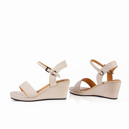A pair of women's wedge sandals in a light beige or cream color, featuring a wide front strap, a thin ankle strap with a silver buckle, and a low wedge heel, shown against a plain white background.