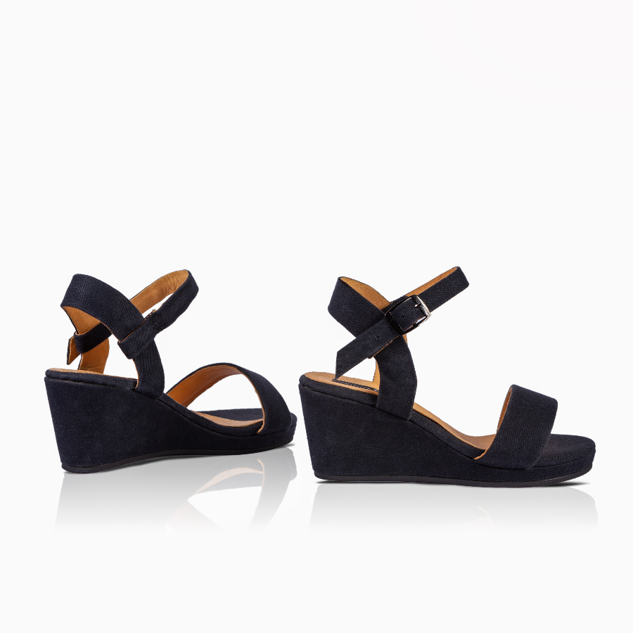 A pair of women's wedge sandals in black, featuring a single wide toe strap, an adjustable ankle strap with a silver buckle, and a low wedge heel, shown against a white background with a soft reflection.