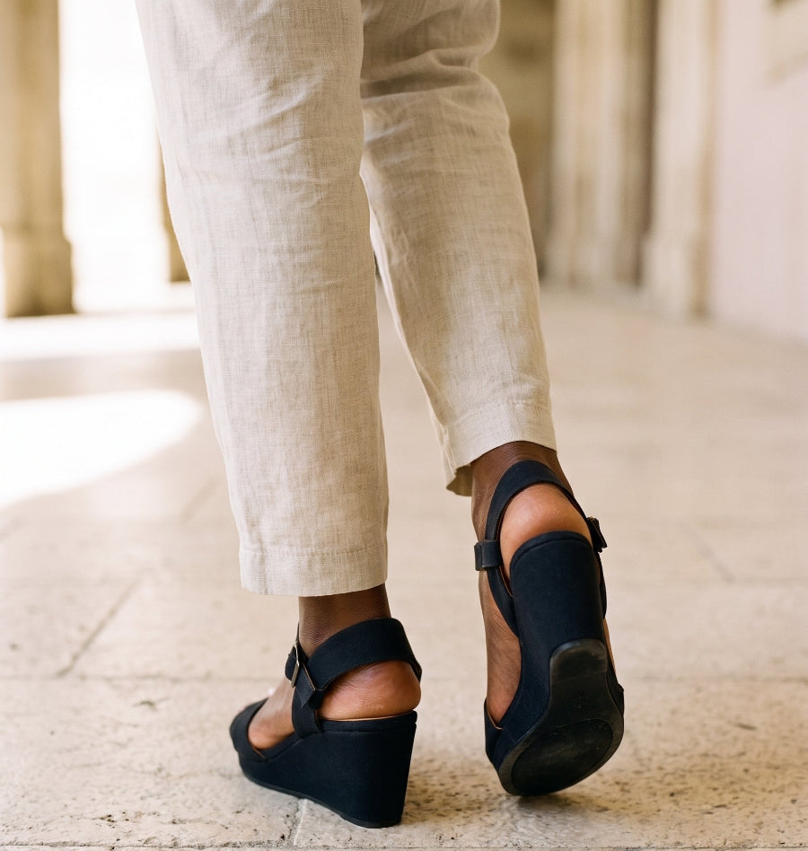 Woman in cream line trousers and black espadrille wedge sandals standing on a stone terrace outdoor setting 
