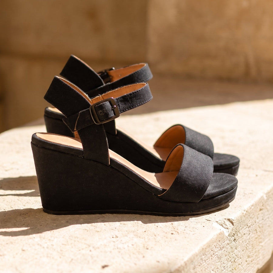 A close up shot of a woman's feet wearing  black espadrille wedge sandals standing on a stone terrace 