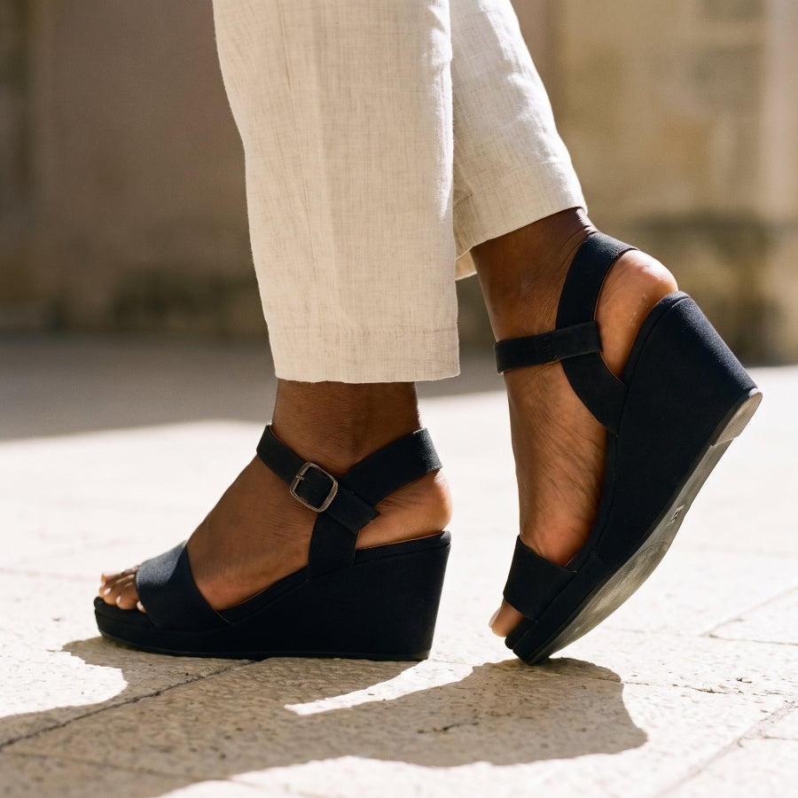 Woman in cream line trousers and black espadrille wedge sandals standing on a stone terrace outdoor setting 