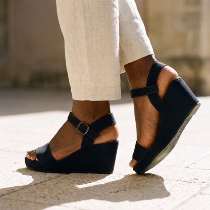 Woman in cream line trousers and black espadrille wedge sandals standing on a stone terrace outdoor setting 