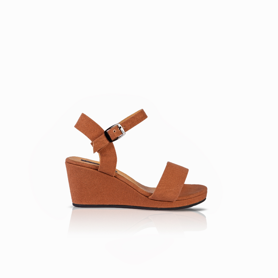 A single women's wedge sandal in a warm tan or cognac brown color, featuring a wedge sole, a wide front strap, and an adjustable ankle strap with a silver buckle, shown from a side profile on a white background.