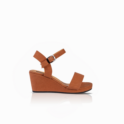 A single women's wedge sandal in a warm tan or cognac brown color, featuring a wedge sole, a wide front strap, and an adjustable ankle strap with a silver buckle, shown from a side profile on a white background.