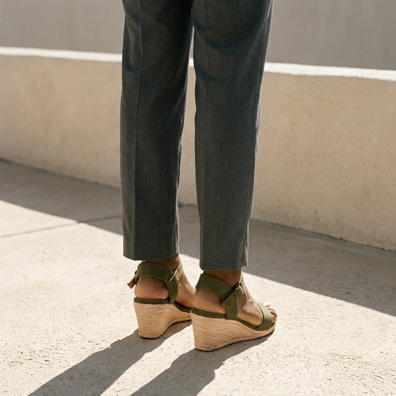 Woman in gray trousers and olive espadrille wedge sandals standing in a stone terrace outdoor setting 