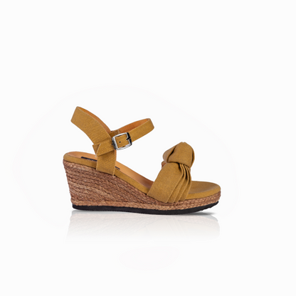 A single women's wedge sandal in mustard with a knotted detail across the instep, an adjustable ankle strap with a silver buckle, and a natural jute-wrapped wedge heel, shown from a side profile on a white background.