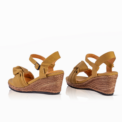 A pair of women's wedge sandals in mustard yellow with braided jute espadrille wedge sandals, shown from a three-quarters angle on a white background.