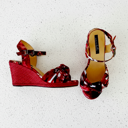 Red esapdrille wedge sandals with a patterned strap on a white textured background
