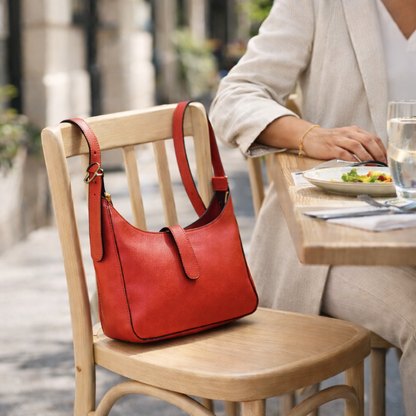 Red leather shoulder bag on a chair with a blurred background of a person dining outdoors.